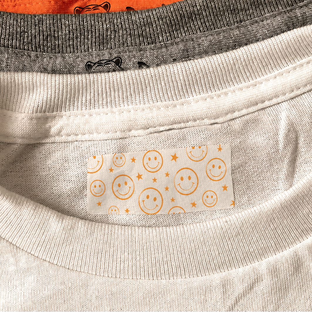 Close-up of a light beige crewneck t-shirt showing a decorative inner neck label with yellow smiley faces and stars, layered over a gray and orange shirt.